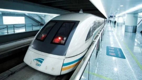 Maglev train stopped at a sleek, modern station platform, showing a streamlined white nose with dark windows and a blue‑and‑orange stripe along the side.