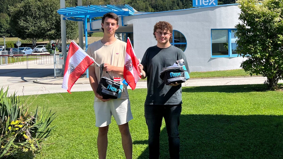 Zwei männliche Lehrlinge stehen zusammen mit österreichischen Flaggen und gewonnenen Preisen von Flex