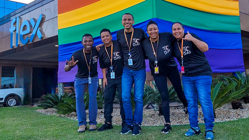 Mitarbeiter von Flex in Brasilien stehen vor einer Pride-Flagge vor dem Gebäude von Flex