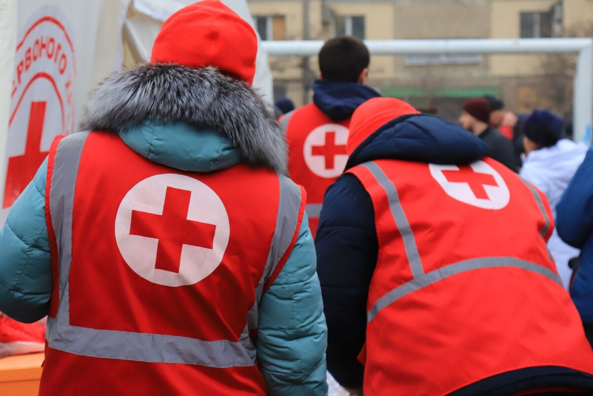 two volunteers wearing red cross vests provide aid