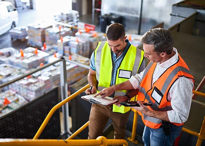 Zwei männliche Mitarbeiter besprechen Auftragsabwicklungs- und Logistikoptionen in einem Lager