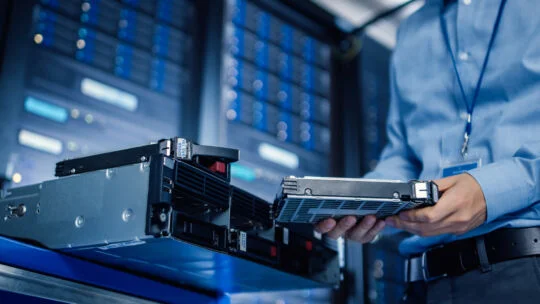 Technician installing a hot-swappable hard drive into a server rack in a data center, showcasing enterprise hardware maintenance and IT infrastructure management.