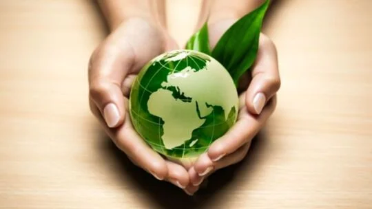 A pair of hands gently holding a green translucent globe with a leaf behind it, symbolizing environmental care and sustainability.
