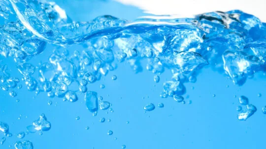 Close‑up view of clear blue water with rising air bubbles and swirling motion near the surface.
