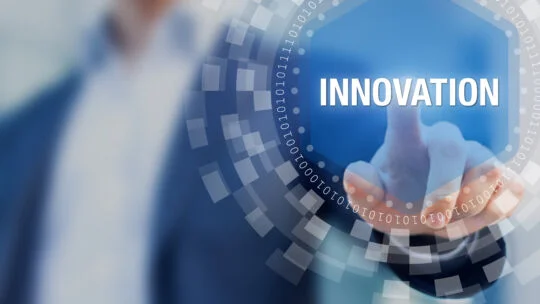 Person in business attire pressing a virtual hexagonal button labeled INNOVATION, surrounded by a circular digital interface with binary code elements.