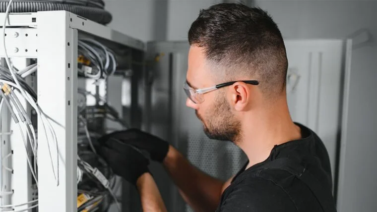 Person demonstrating worker safety in AI data centers by wearing safety glasses and gloves working on electrical wiring