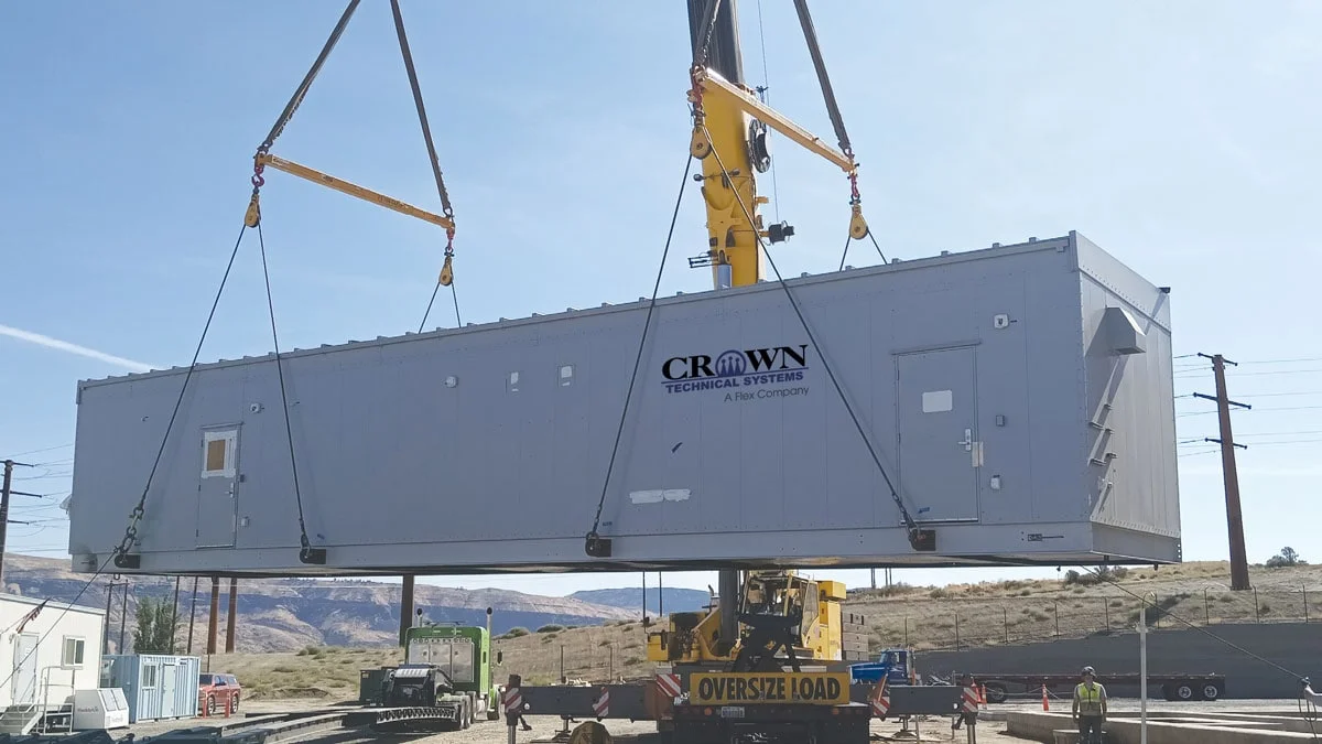 Modular enclosure from Crown Technical Systems, a Flex company, on a crane being lowered into position onsite